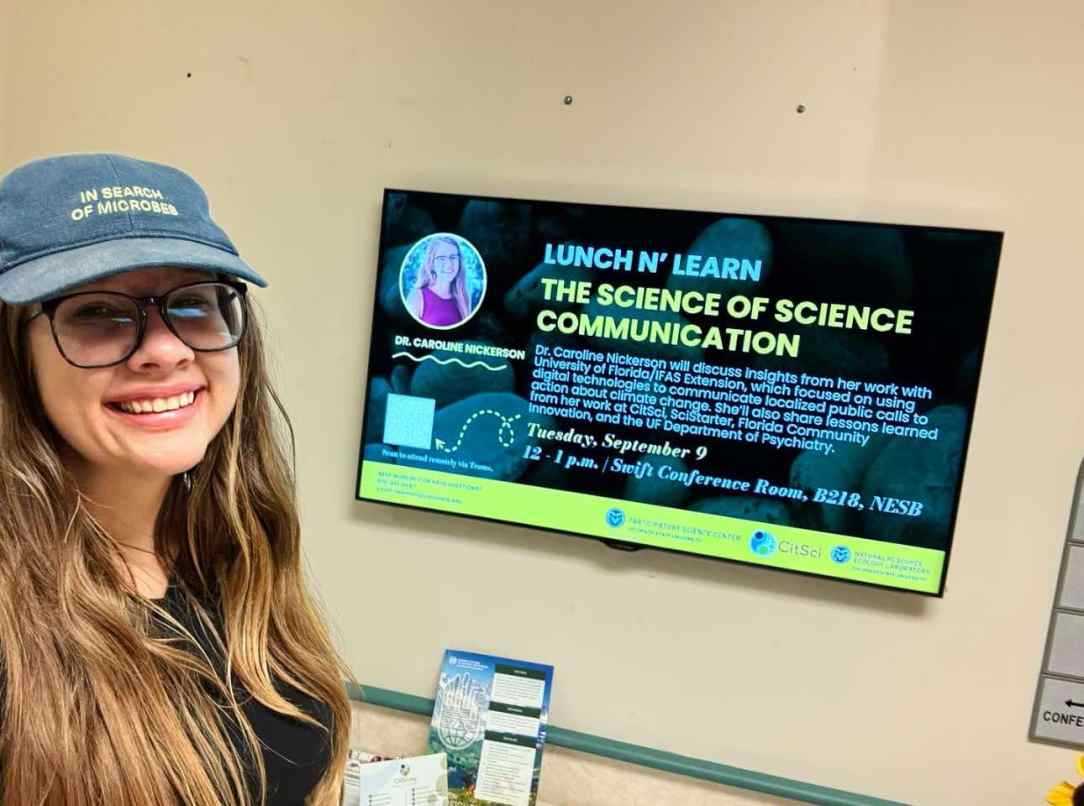 Image of Caroline smiling in front of a poster advertising her talk